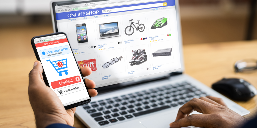 A laptop on a table with an online store page open. A smartphone displaying a shopping cart is in the left corner of the picture. 