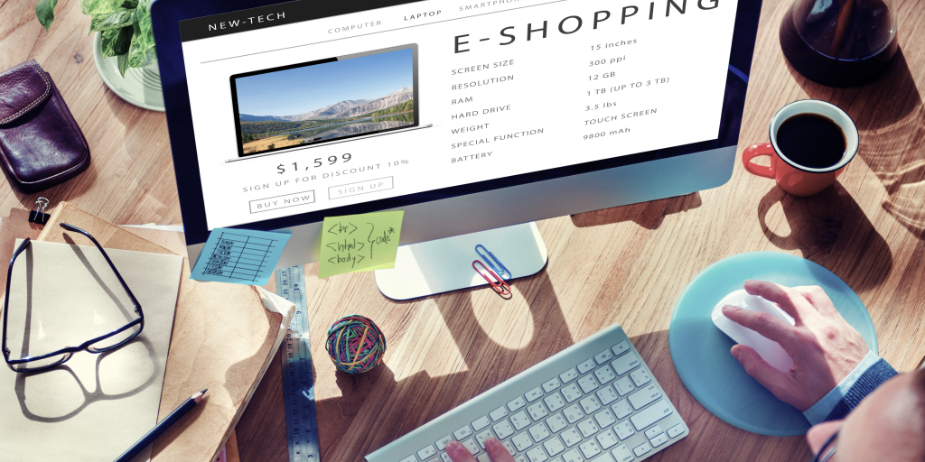 A bird's eye view of a computer display and a keyboard with several sticky notes attached to its lower end. Words E-SHOPPING are displayed on the screen along with the price, a laptop and product specifications. 