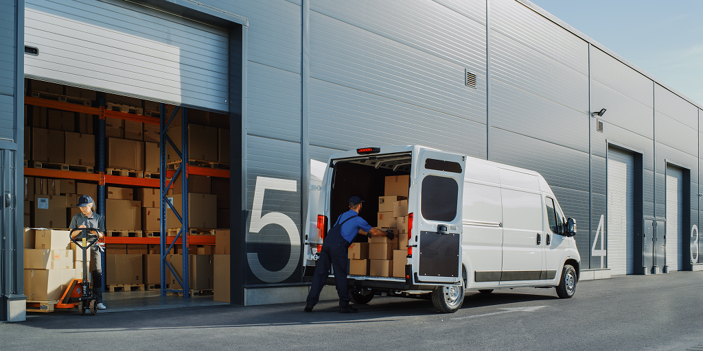 A worker loading packages onto a truck in front of a warehouse. 