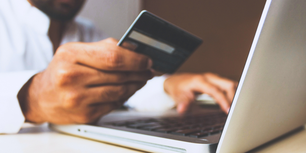 A man holding a credit card in one hand and typing on a laptop with the other. 