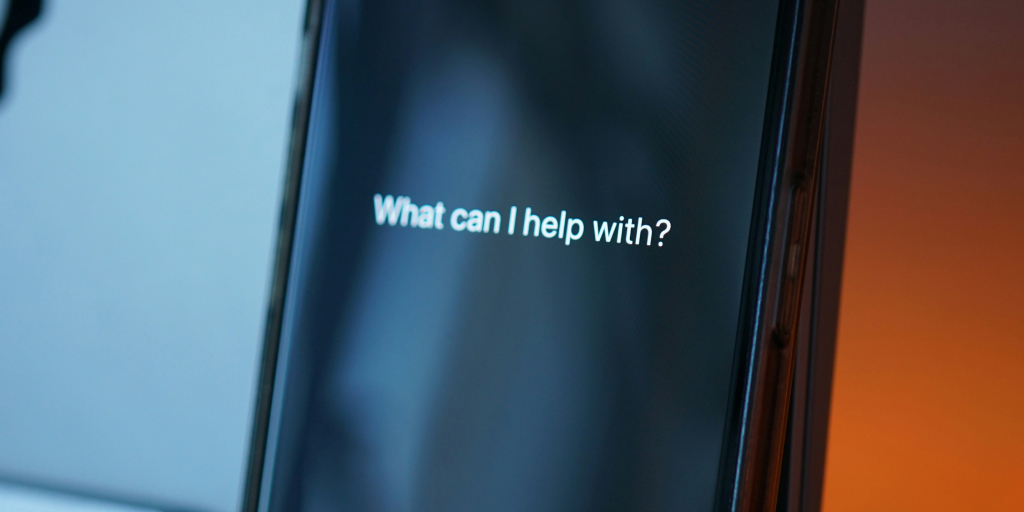 A close-up view of a smartphone with the words 'What can I help with?' displayed on its screen.