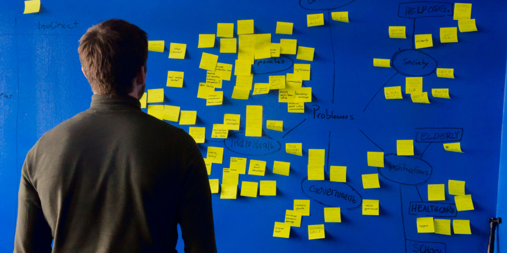 A man standing in front of a blue board with multiple stick-it notes.