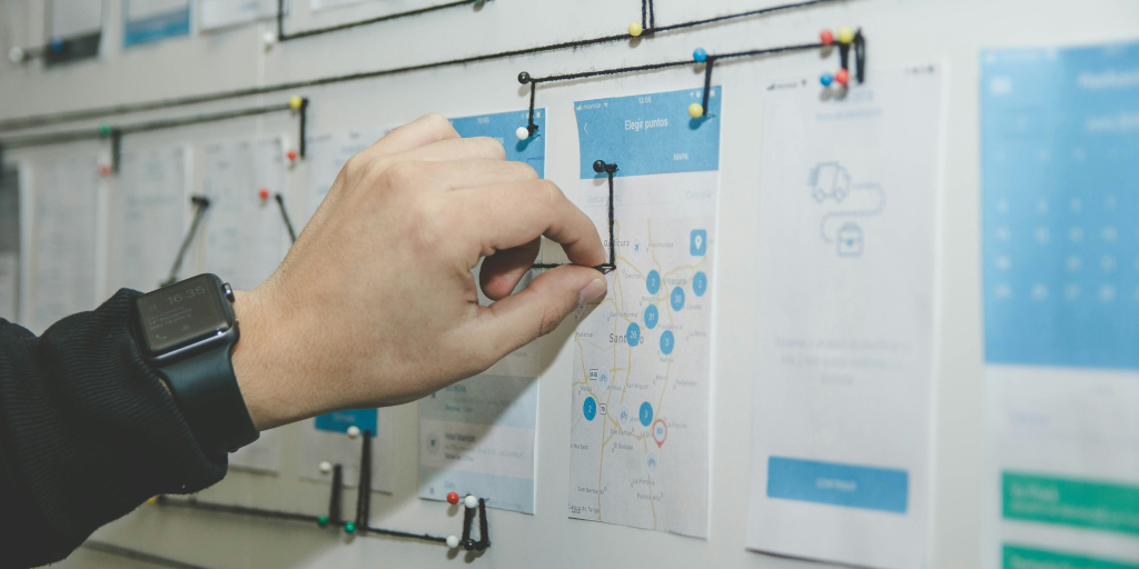 A man sticking a pin into a board with multiple pins connected  by threads. 