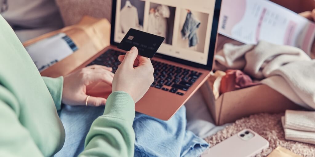 A person holding a debit card in their right hand. They have a computer on their lap and their left arm in on the touchpad.