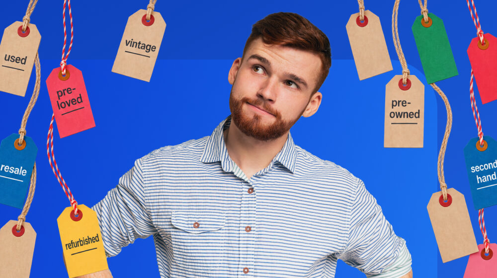 A young man in front of a monochrome blue background. All around him are price tags hanging from ropes with words 'Vintage', Used, and 'Pre-owned' on them.